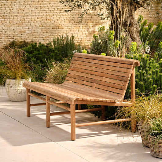 Wooden bench in a garden setting with plants and a stone wall.
